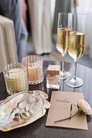Foto de Composición de la boda con dos cócteles, flautas de champán, botella de aroma, invitación en sobre, rosa blanca fresca y anillos en concha de perlas - Imagen libre de derechos
