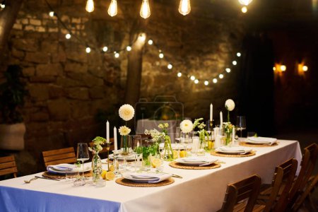 Téléchargez les photos : Table de fête servie avec assiettes, verres à vin, décorations et serviettes debout au mur de pierre dans le restaurant avec des illuminations - en image libre de droit