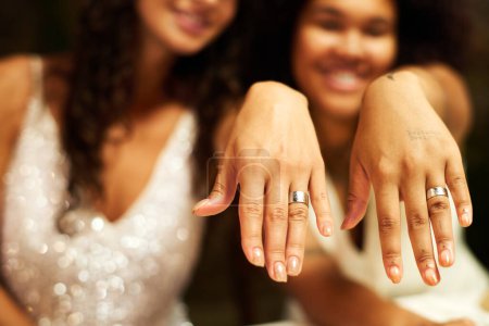 Téléchargez les photos : Mains de deux jeunes filles gays interculturelles montrant leurs alliances après s'être mariées tout en étant assis devant la caméra - en image libre de droit