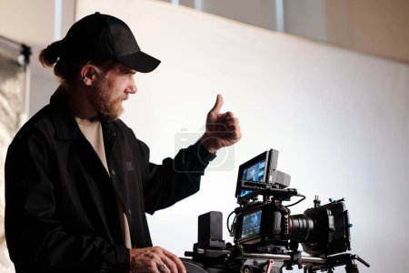 Photo for Director of production studio or crew showing thumb up gesture to his team while standing in front of steadicam during shooting - Royalty Free Image