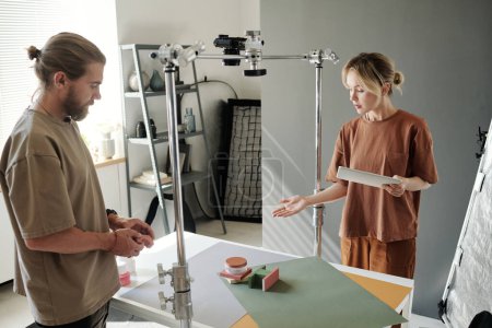 Foto de Mujer joven con tableta apuntando a la composición con objetos sobre la mesa mientras la presenta al fotógrafo antes de disparar - Imagen libre de derechos