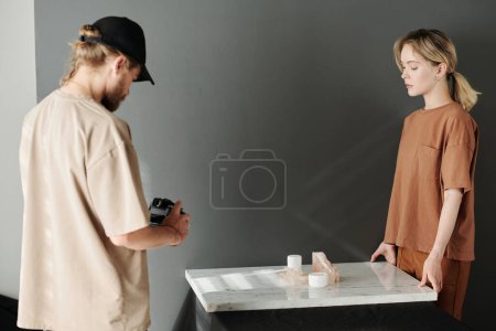 Photo for Young man with photocamera taking photos of composition on marble platform while his assistant standing in front of him - Royalty Free Image