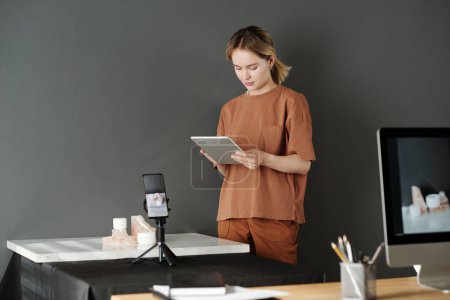 Téléchargez les photos : Jeune femme en casual utilisant la tablette tout en se tenant devant le lieu de travail avec la composition sur la plate-forme de marbre - en image libre de droit
