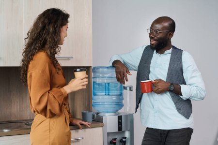 Photo for Happy young intercultural office workers chatting and having tea and coffee at break while standing by water dispenser with gallon - Royalty Free Image