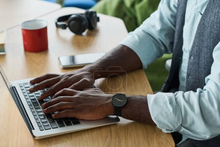 Foto de Manos de joven elegante empresario afroamericano sobre teclado portátil sentado por el lugar de trabajo en la oficina y trabajando en la red - Imagen libre de derechos