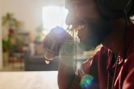 Foto de Primer plano de un joven alegre hombre multiétnico con barba sujetada por un micrófono mientras especula o habla con el huésped en el estudio - Imagen libre de derechos