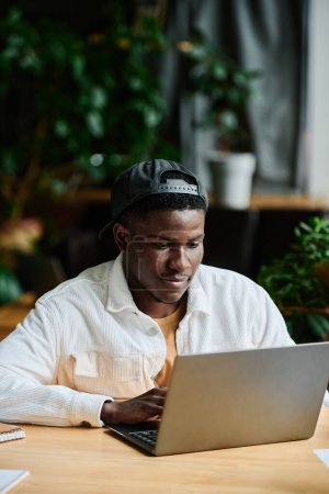 Foto de Joven hombre de negocios afroamericano que se concentra en el trabajo con datos en línea mientras se sienta frente a la computadora portátil y prepara la presentación - Imagen libre de derechos