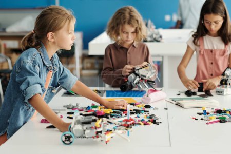 Photo for Group of youthful schoolkids standing by table with details of constructor and creating new robots during individual work at lesson - Royalty Free Image