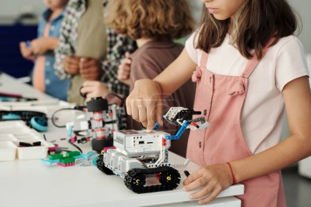 Photo for Close-up of youthful schoolgirl pressing start button on top of toy robot which she constructed at lesson of robotics at school - Royalty Free Image