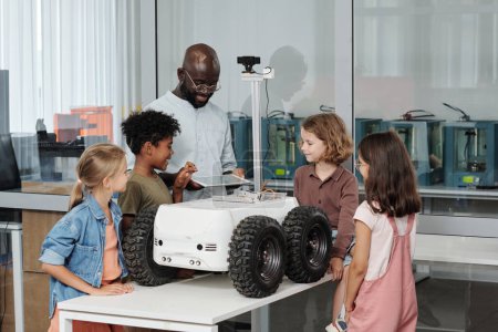 Photo for Group of clever intercultural pupils and their teacher of robotics using tablet for remote control of crawler created in school laboratory - Royalty Free Image