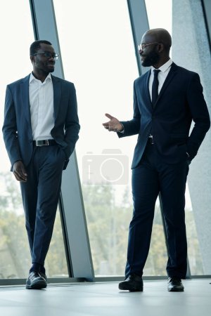 Téléchargez les photos : Homme d'affaires afro-américain confiant en costume parler à son collègue et lui expliquer les points les plus importants du contrat de partenariat - en image libre de droit