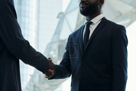 Photo for Cropped shot of young African American businessman in dark blue suit handshaking with new business partner after negotiating - Royalty Free Image