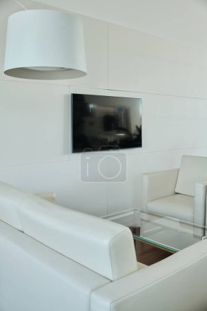 Téléchargez les photos : Partie de la zone de recharge dans un bureau moderne à aire ouverte avec canapé en cuir blanc et fauteuil entourant une petite table en verre par mur - en image libre de droit