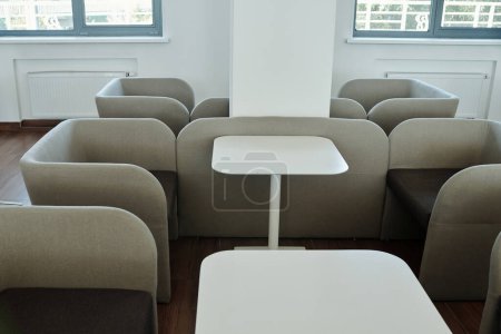 Photo for Group of comfortable grey velvet armchairs and small white square tables standing in spacious openspace office and forming recharge zone - Royalty Free Image