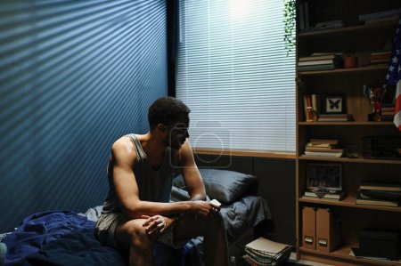 Photo for Young sleepless man in underwear and eyeglasses sitting on bed at midnight and suffering from post traumatic syndrome - Royalty Free Image