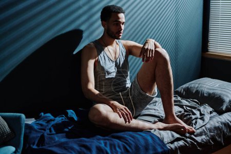 Téléchargez les photos : Jeune homme sans sommeil en sous-vêtements assis sur le lit dans la chambre noire à minuit et souffrant du syndrome post-traumatique - en image libre de droit