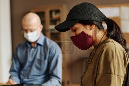 Photo for Side view of young upset woman in protective mask and baseball cap sharing her traumatic experience with support group at session - Royalty Free Image