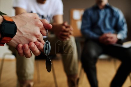 Photo for Hands with clasped fingers of young depressed man with two medallions on chain sitting among attendants of psychological session - Royalty Free Image