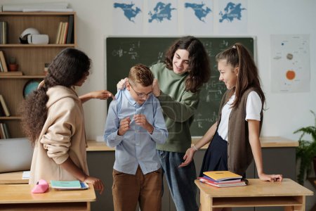 Photo for Group of classmates surrounding junior schoolboy and mocking at him while pre-teen guy holding him by back of shirt - Royalty Free Image