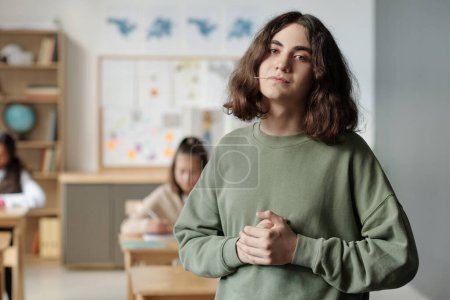 Photo for Pre-teen confident and impudent guy with toothpick in mouth looking at camera while standing against his classmates in classroom - Royalty Free Image