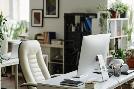Photo for Computer monitor standing on workplace of office worker with notebook and other supplies and white leather armchair near by - Royalty Free Image