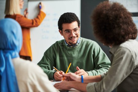Photo for Happy young man in eyeglasses communicating with another student at break between lessons against teacher preparing for presentation - Royalty Free Image