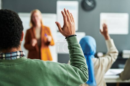 Photo for Part of back of young male student in green pullover raising hand at lesson to ask question to teacher or give his answer - Royalty Free Image