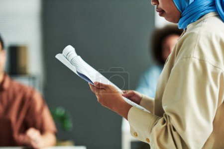 Photo for Close-up of young Muslim female speaker with document making report at conference or seminar while standing against audience - Royalty Free Image