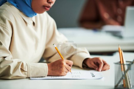 Téléchargez les photos : Main de la jeune étudiante musulmane avec crayon sur papier avec test de grammaire cochant les bonnes réponses pendant le travail individuel - en image libre de droit
