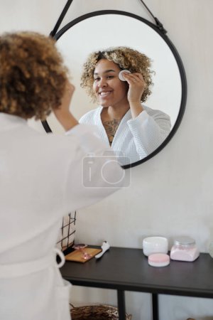 Téléchargez les photos : Joyeux jeune belle femme avec coton tampon application hydratant toner visage après nettoyage visage avec un produit cosmétique purifiant - en image libre de droit