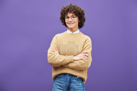 Téléchargez les photos : Jeune femme brune souriante aux lunettes, jean bleu et pull tricoté beige croisant les bras par la poitrine et regardant la caméra isolée - en image libre de droit