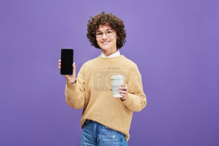 Téléchargez les photos : Joyeux jeune femme brune avec tasse de café montrant smartphone avec écran vide où vous pouvez placer le texte de la publicité - en image libre de droit