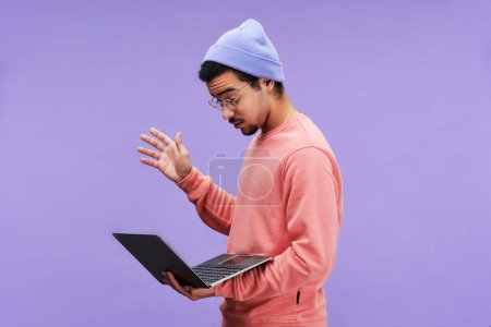 Foto de Vista lateral de un joven programador masculino sorprendido en ropa casual y anteojos mirando a la pantalla del ordenador portátil mientras se enfrenta a un problema técnico - Imagen libre de derechos