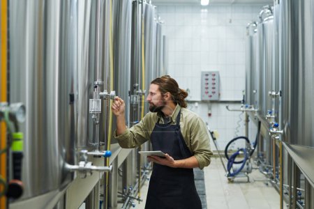 Téléchargez les photos : Travailleur de brasserie vérifiant indicateur de pression sur chaque réservoir avec de la bière - en image libre de droit