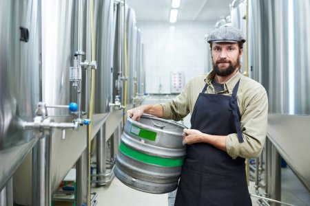 Téléchargez les photos : Portrait d'un travailleur de la fabrication de bière tenant un fût et regardant une caméra - en image libre de droit