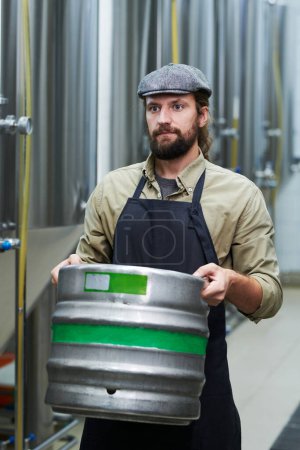 Téléchargez les photos : Portrait du travailleur de la microbrasserie transportant du fût avec de la bière à l'entrepôt - en image libre de droit