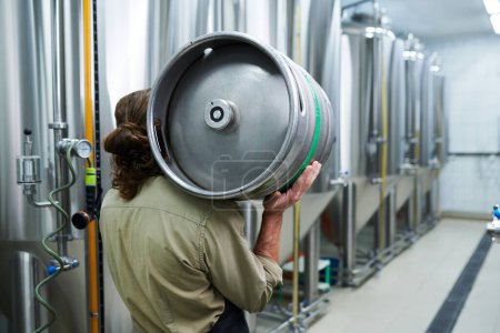 Téléchargez les photos : Ouvrier de microbrasserie transportant un fût de bière à l'entrepôt, vue de dos - en image libre de droit