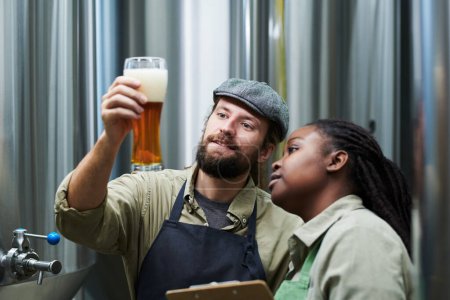 Téléchargez les photos : Travailleurs souriants de brasserie vérifiant l'épaisseur de la mousse de bière - en image libre de droit