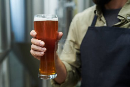 Téléchargez les photos : Ouvrier tenant un grand verre de bière produite dans une microbrasserie - en image libre de droit