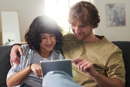 Téléchargez les photos : Jeune homme et femme souriant à la recherche d'un film en ligne intéressant tout en se relaxant sur le canapé et en pensant à la façon de passer des loisirs - en image libre de droit