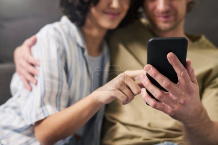 Téléchargez les photos : Focus sélectif sur les mains des jeunes couples avec smartphone choisir de la nourriture pour le déjeuner dans le menu en ligne tout en se relaxant à la maison le week-end - en image libre de droit