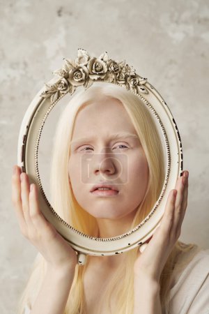 Photo for Face of young serene albino woman in oval antique frame decorated with roses during stylish photo session in studio with marble walls - Royalty Free Image