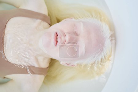 Photo for Above shot of young natural albino woman wearing beige tanktop lying in bathtub full of clear water and relaxing during photo shooting - Royalty Free Image