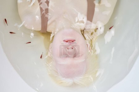 Foto de Sobre el ángulo de la joven mujer albina pacífica con los ojos cerrados en la bañera llena de agua pura y un grupo de pequeños peces decorativos - Imagen libre de derechos