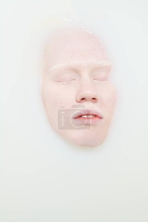 Téléchargez les photos : Angle supérieur du visage de la jeune femme albinos avec les yeux fermés bénéficiant d'une procédure d'hygiène tout en étant couché dans la baignoire avec du lait chaud et de l'eau - en image libre de droit