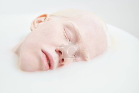 Photo for Part of face of peaceful or sleeping albino girl keeping her eyes closed while lying in bathtub filled with warm water and milk - Royalty Free Image