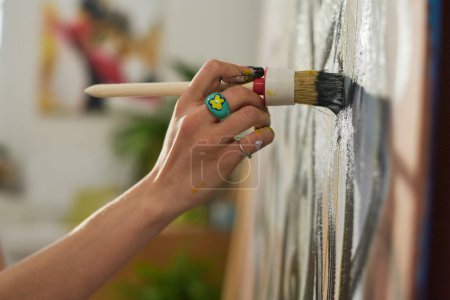 Téléchargez les photos : Main de jeune artiste féminine avec pinceau lors de la création de nouvelles œuvres d'art en home studio ou atelier et une partie de son chef-d'œuvre - en image libre de droit