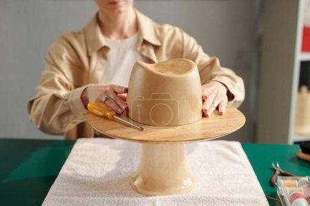 Photo for Close-up of wooden hat workpiece on table against young creative craftswoman working over new model for client of her studio - Royalty Free Image