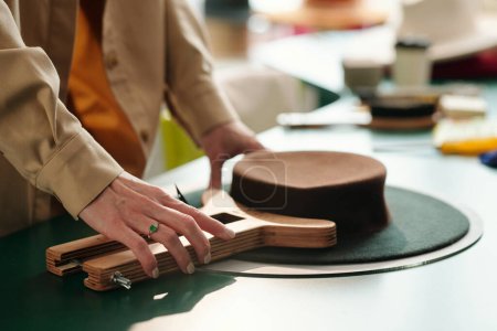 Téléchargez les photos : Vue latérale de la main de l'artisan en utilisant un outil en bois pour façonner la partie supérieure du chapeau de porc tout en créant un nouvel article à vendre dans un magasin d'artisanat - en image libre de droit