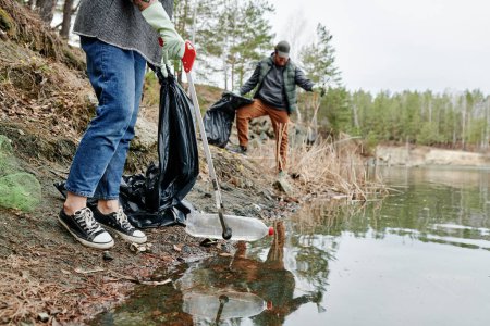 Couple cleaning pond in city park from trash and putting garbage in plastic bags